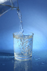 Pour water from  pitcher into  glass, on dark blue background