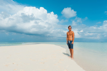 Attractive male looks around standing on beautiful beach with wh