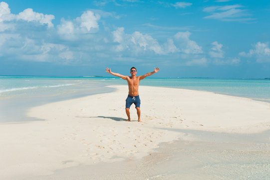 Happy attractive young male jumps on beach with white sand and o