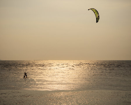 man with kite surving standing in sea water against evening sun