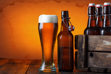 Beer glass with wooden crate full of beer bottles on table