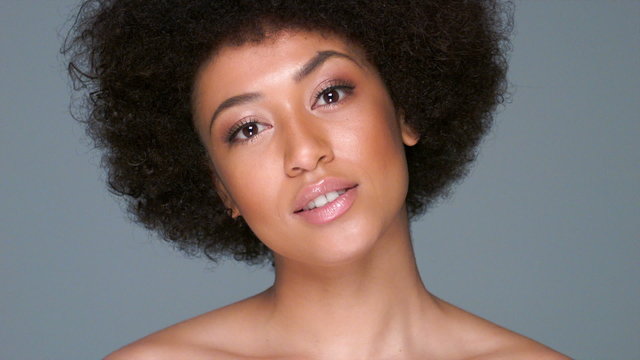 Beautiful Young African American woman with an afro hairstyle and bare shoulders on a grey studio background