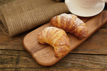 Two croissants with powder sugar on a wooden board