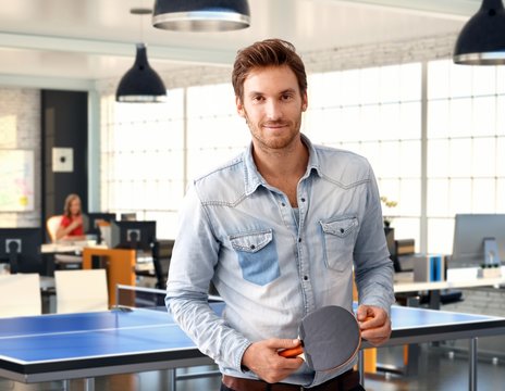 Casual man holding ping-pong racket at office