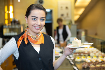 Waitress presenting cake in cafe or confectionery