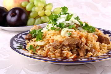 Uzbek pilaf in traditional dishes, fruits in background