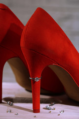 Beautiful ring on heel of red female shoe, on wooden background