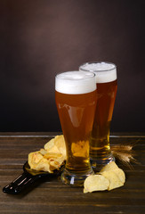 Glasses of beer with snack on table on dark background