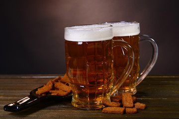 Glasses of beer with snack on table on dark background