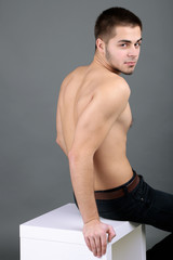 Handsome young sitting on cube on gray background