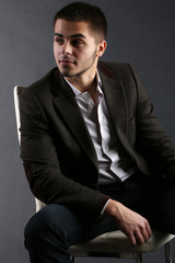 Handsome young sitting on chair on dark background