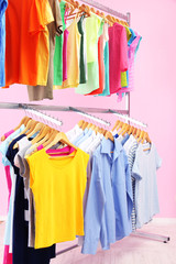 Fototapeta premium Different clothes on hangers, on pink background