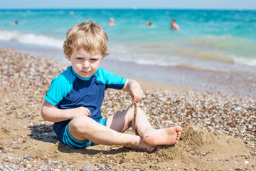 Fototapeta na wymiar Little toddler boy playing with sand and stones on the beach