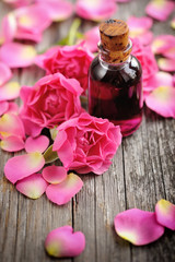 Essential oil with rose petals on wooden background