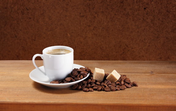 Coffee cup on saucer, beans and sugar on a wooden table
