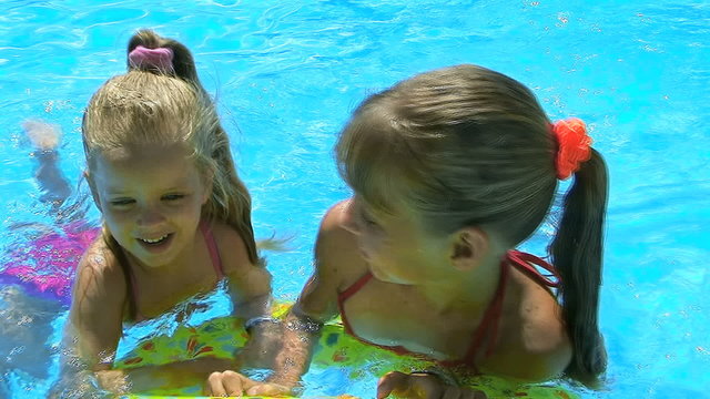 Children sitting on inflatable ring in swimming pool.
