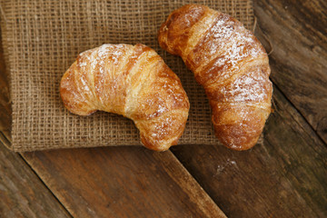 Two sugar powder croissants on a wooden suface