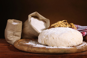 Dough and bags with flour on wooden table on brown background