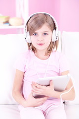 Naklejka premium Little girl sitting on sofa and listening music in room