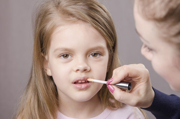 Визажист наносит блеск на губы девочки