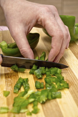 Woman hand cutting a green pepper in kitchen.
