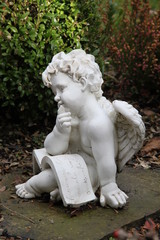 Nachdenklicher Engel mit Buch sitzt auf Grab