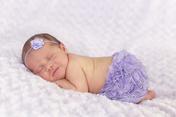 Newborn Mädchen in Bauchlage mit Haarband und Hose