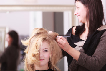 Smiling girl with blond wavy hair by hairdresser in beauty salon