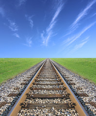 Railway track, green grass and blue sky on the horizon