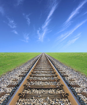 Railway track, green grass and blue sky on the horizon