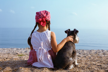 beautiful little girls embracing her dog looking at the sea