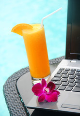 Black laptop and orange juice poolside