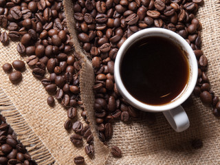 white cup with coffee on burlap background with beans