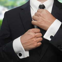 a man in a black suit straightens his tie