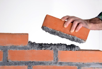 Constructor sujetando un ladrillo construyendo un muro.