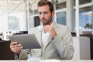 Fototapeta premium Handsome young businessman working on tablet drinking espresso