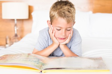 Happy blonde boy lying on bed reading a storybook