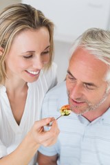 Happy woman feeding her partner a spoon of vegetables