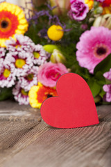 Rotes Herz und ein bunter Blumenstrauß auf Holztisch