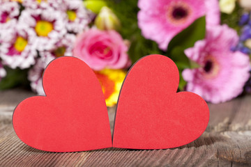 Fototapeta na wymiar Zwei roten Herzen mit buntem Blumenstrauß im Hintergrund