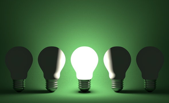 Glowing light bulb in row of switched off ones on green