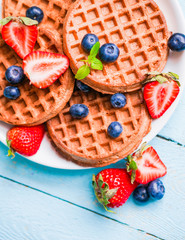 Whole grain waffles with berries on blue wooden background