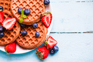 Whole grain waffles with berries on blue wooden background