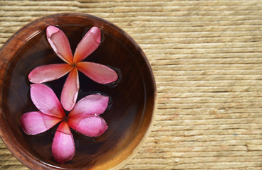 Obraz na płótnie Canvas Two Pink frangipani in water wooden bowl on Brown straw mat