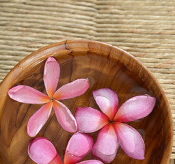 Three frangipani in water wooden bowl on Brown straw mat