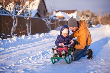 Young dad sledding his little adorable daughter on a sunny