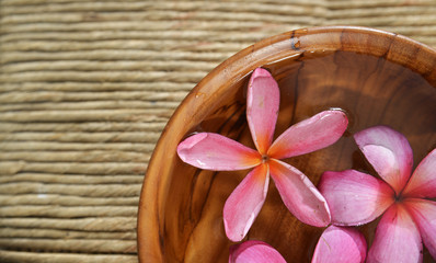 Three frangipani in water wooden bowl on Brown straw mat