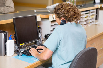 Nurse Answering Telephone While Working On Computer At Reception