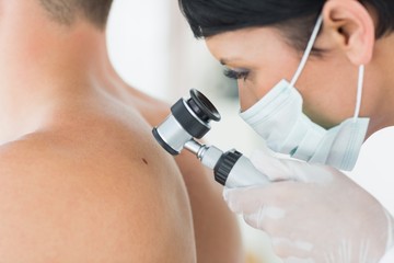 Dermatologist examining mole on patient - obrazy, fototapety, plakaty