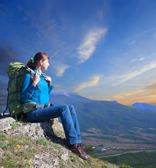 Woman with backpack enjoying sunset on top of mountain